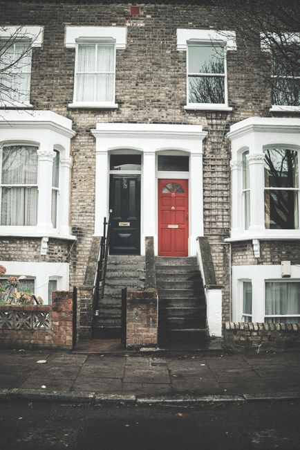 A row of multi-storey Victorian terraced houses in London with colorful facades in shades of blue, pink, and cream, featuring large bay windows with white frames and decorative mouldings. The building